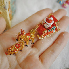 Hand holding a miniature beaded Santa Claus figure with reindeer on a light background