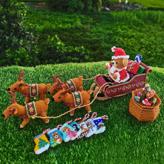 Beaded scene with a teddy bear in a sleigh pulled by reindeer on grass.