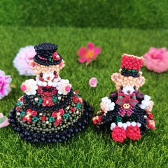 Two handmade bear figurines made of beads with black wedding dress on a grassy background with flowers.