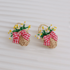 Pair of woven earrings with red and white checkered ribbons and small flowers on a light background