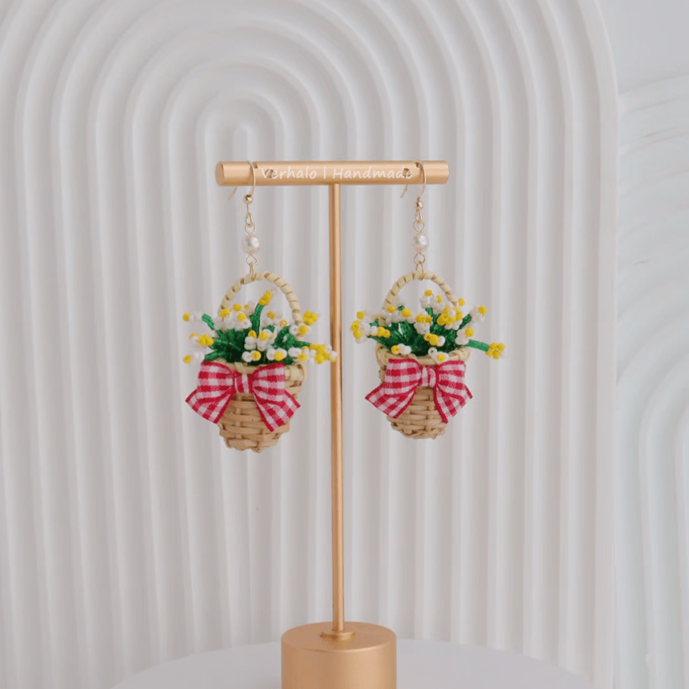 Earrings with floral designs and ribbons on a gold stand against a white background