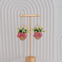 Earrings with floral designs and ribbons on a gold stand against a white background