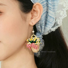 Close-up of a person wearing a decorative earring with a basket and bow design.