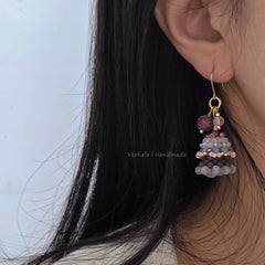 Close-up of an earring with beads worn by a person with black hair against a light blue background.