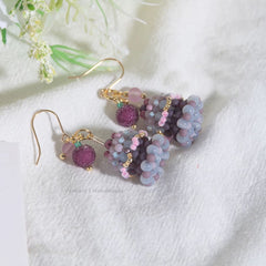 Beaded birthday cake earrings on a white fabric background with floral elements.