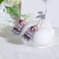Pair of beaded birthday cake earrings on a white heart-shaped stand with floral background