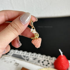 Hand holding a beaded strawberry charm with a black background