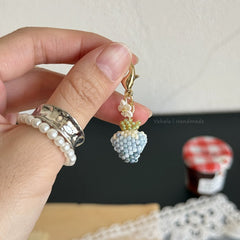 Hand holding a beaded keychain with a small plant design against a neutral background