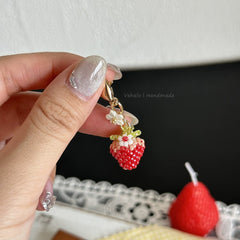 Hand holding a beaded strawberry charm with a blurred background