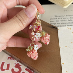 Hand holding a decorative keychain with strawberry and flower charms on a book background