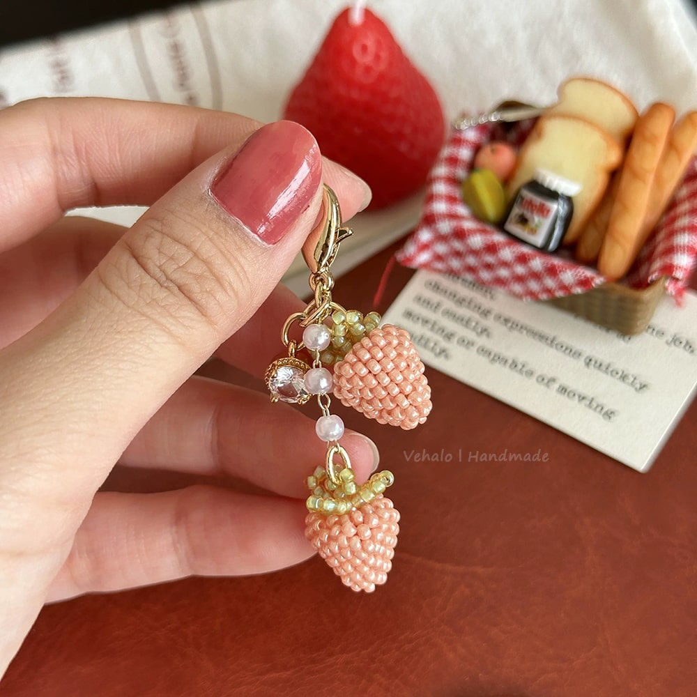 Hand holding a strawberry-shaped bag cham with beads against a blurred background