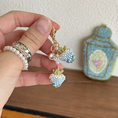 Hand holding a colorful keychain with beads and charms, with a needlepoint item in the background.