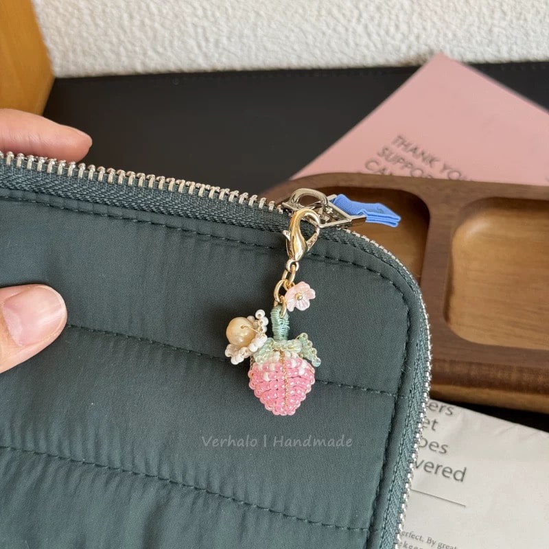 Green wallet with a decorative charm featuring a pink strawberry and a small figure, held by a hand.