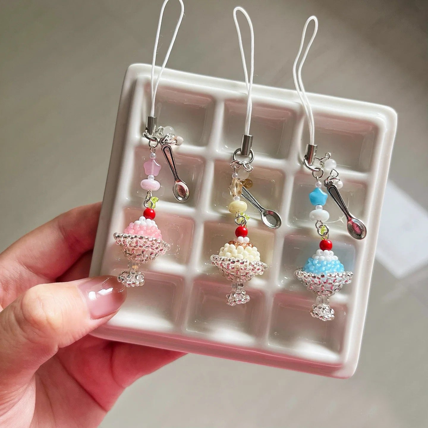 Three decorative pudding cake phone charms on a clear display card held by a hand.
