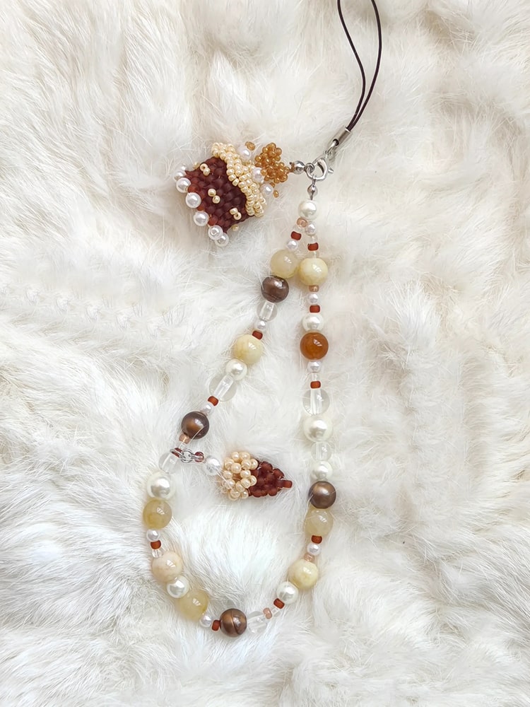 Beaded cake phone strap with floral elements on a white fur background