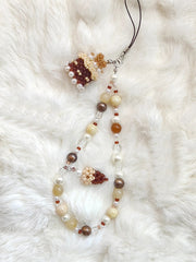 Beaded cake phone strap with floral elements on a white fur background