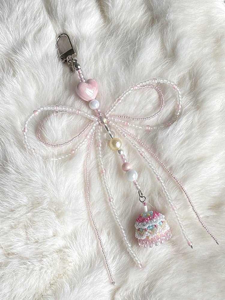 Decorative keychain with a bow and small cake charm on a fluffy white surface