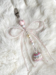 Decorative keychain with a bow and small cake charm on a fluffy white surface