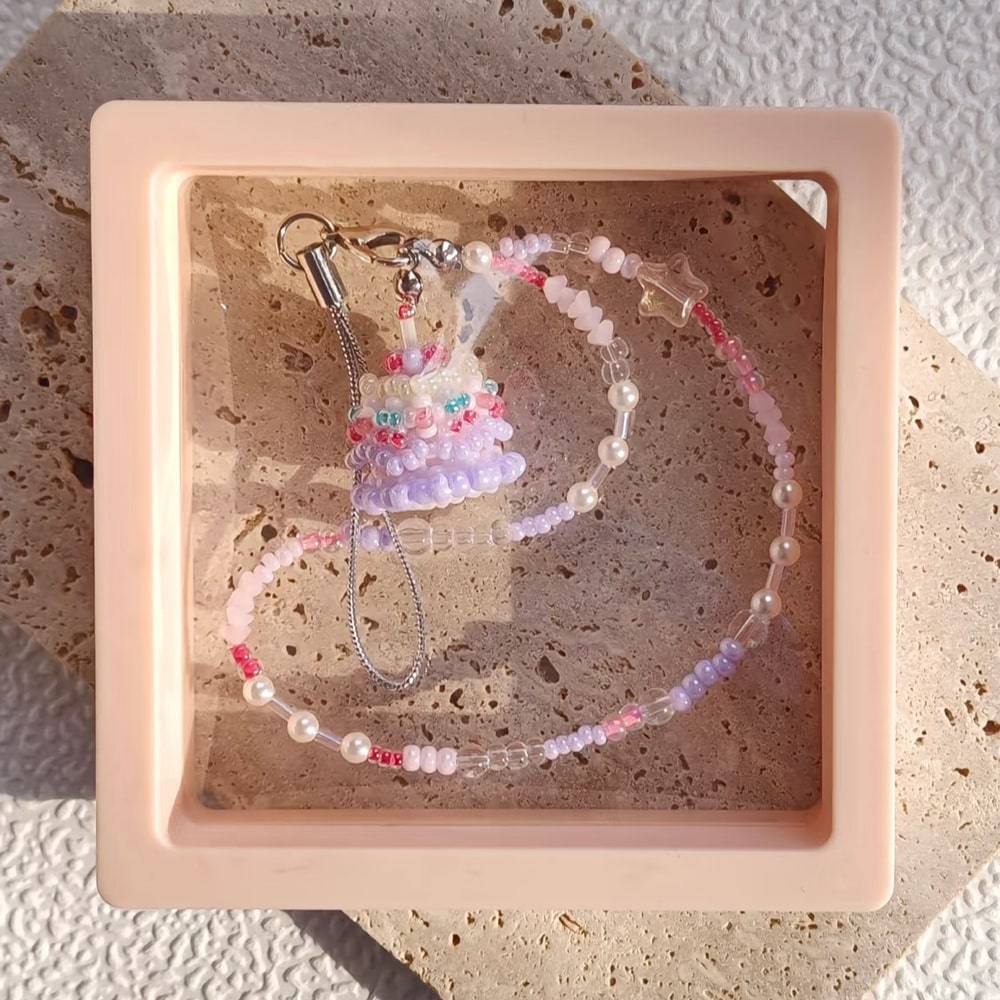 Beaded phne strap with a small birthday cake pendant in a pink display box.