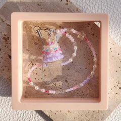 Beaded phne strap with a small birthday cake pendant in a pink display box.