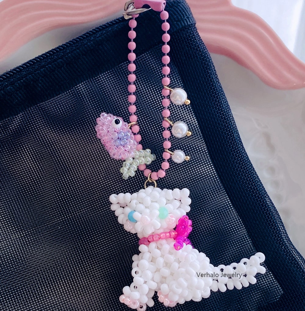 Beaded white cat charm with pink bow on a dark blue background丨Verhal Custom Jewelry