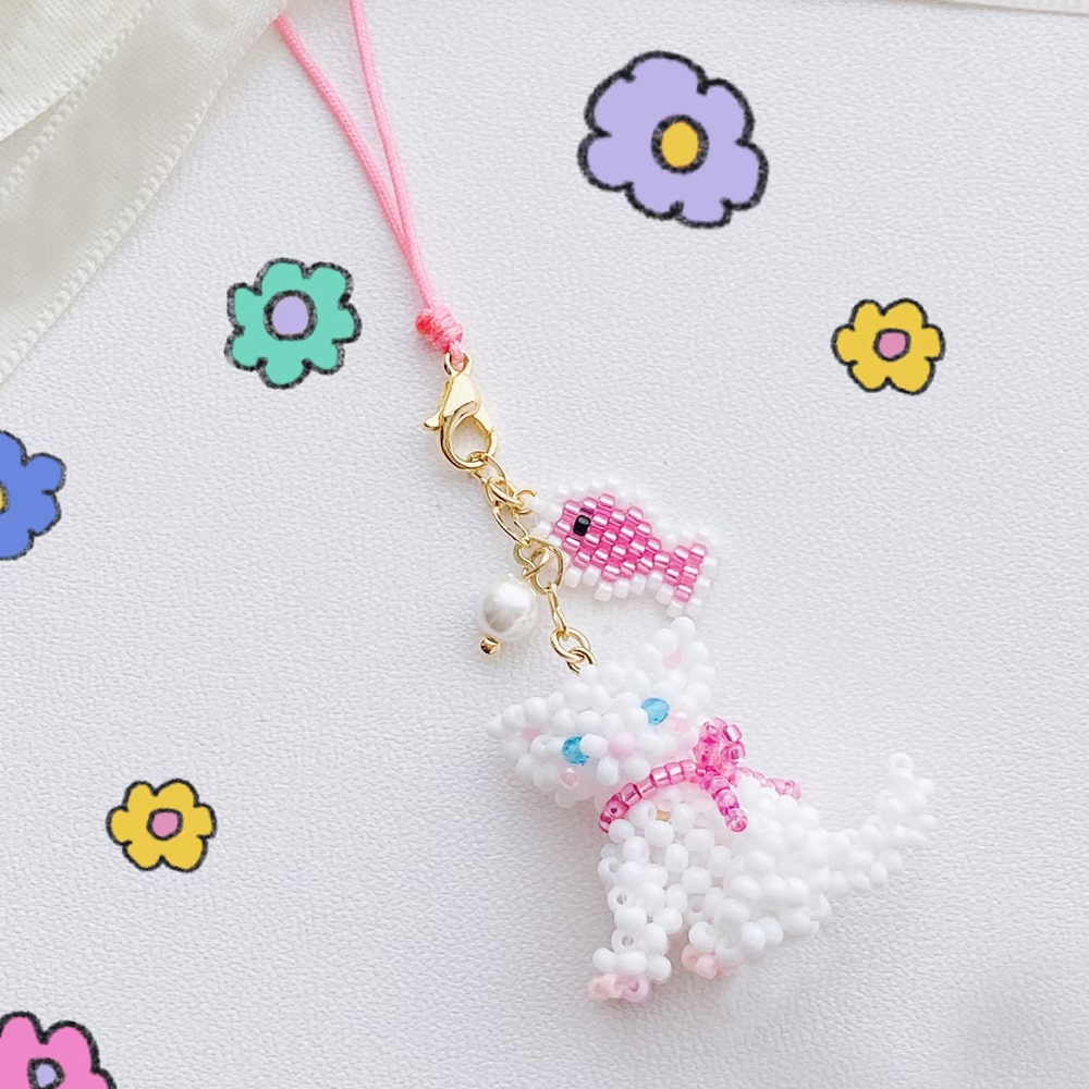 Beaded charm shaped like a cat with a pink bow on a white background with colorful flowers.