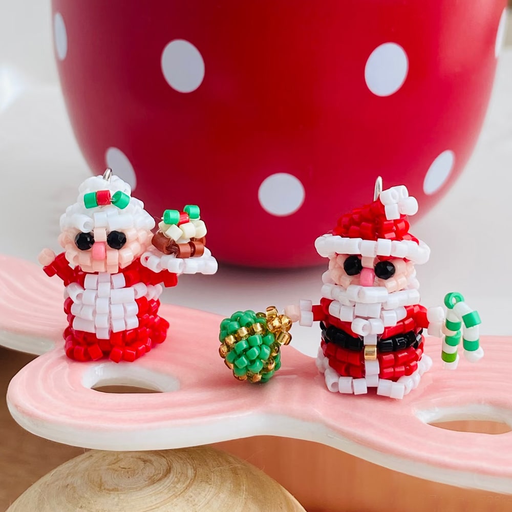 Handmade two small Santa Claus figurines with a red polka dot cup in the background - verhalojewelry