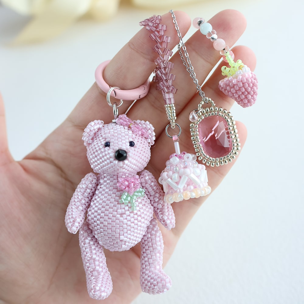 Hand holding a pink beaded teddy bear keychain with accessories on a light background - Verhalo jewelry