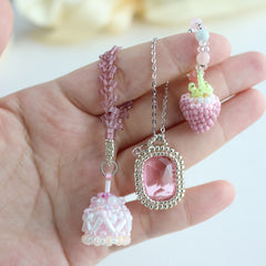 Hand holding three pink beaded charms against a blurred background - Verhalo jewelry