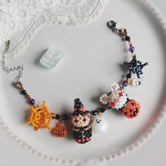 Halloween-themed beaded bracelet with witch, pumpkin, and spider charms on a white lace background. - Verhalo handmade jewelry