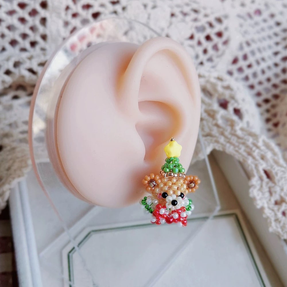 Close-up of an ear with a Christmas  Stud earring shaped like a bear in a Christmas tree outfit.