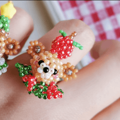 Close-up of a hand wearing a beaded ring with a bear design and red apple.