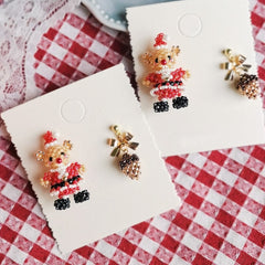 Earrings shaped like teddy bears in Santa outfits on a red and white checkered background
