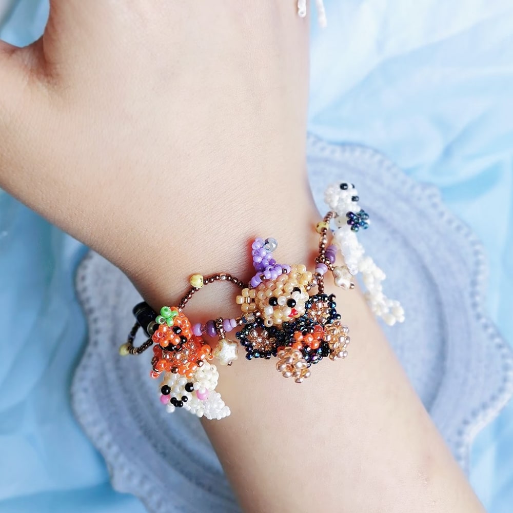 Hand wearing a colorful beaded bracelet with character design on a light blue fabric background
