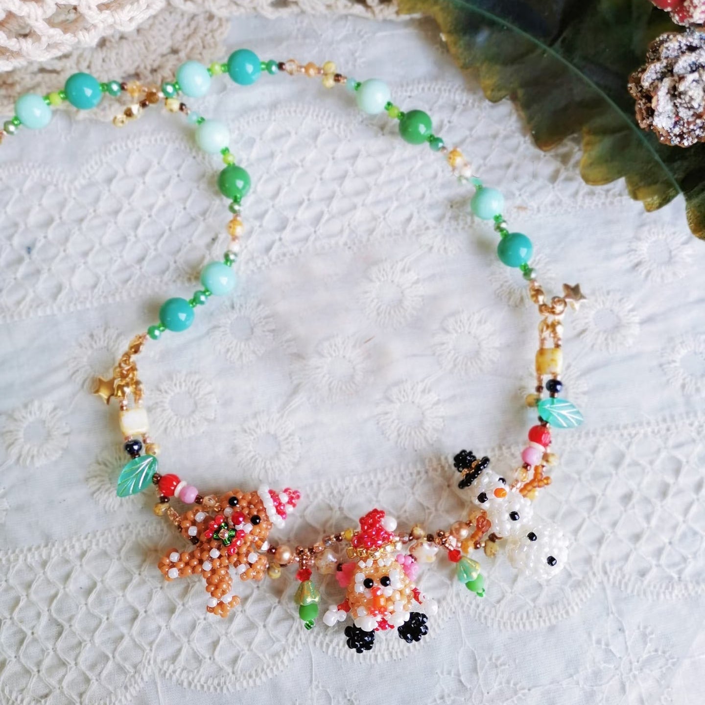 Handmade Colorful beaded Christmas spirit necklace with snowman, Santa,  Gingerbread Man figures on a textured white surface- verhalo custom jewelry