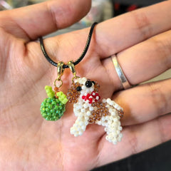 Hand holding a beaded dog pendant with a green apple on a black cord - verhalo custom jewelry