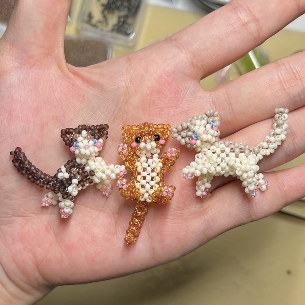 beaded three small cat figurines made of beads held in a hand- verhalo custom jewelry