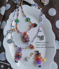 Colorful beaded necklace with magic girl pendants on a white dish.- verhalo custom jewelry