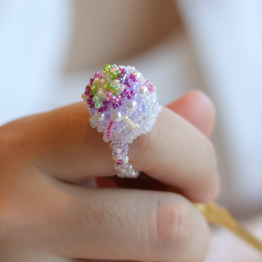 Colorful beaded cake ring on a finger with a blurred background