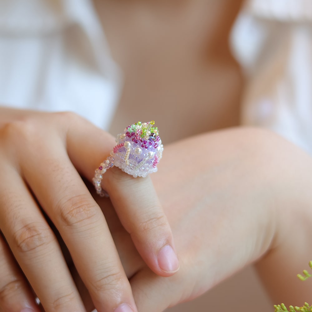 Close-up of a hand wearing a decorative cake ring with gemstones on a blurred background