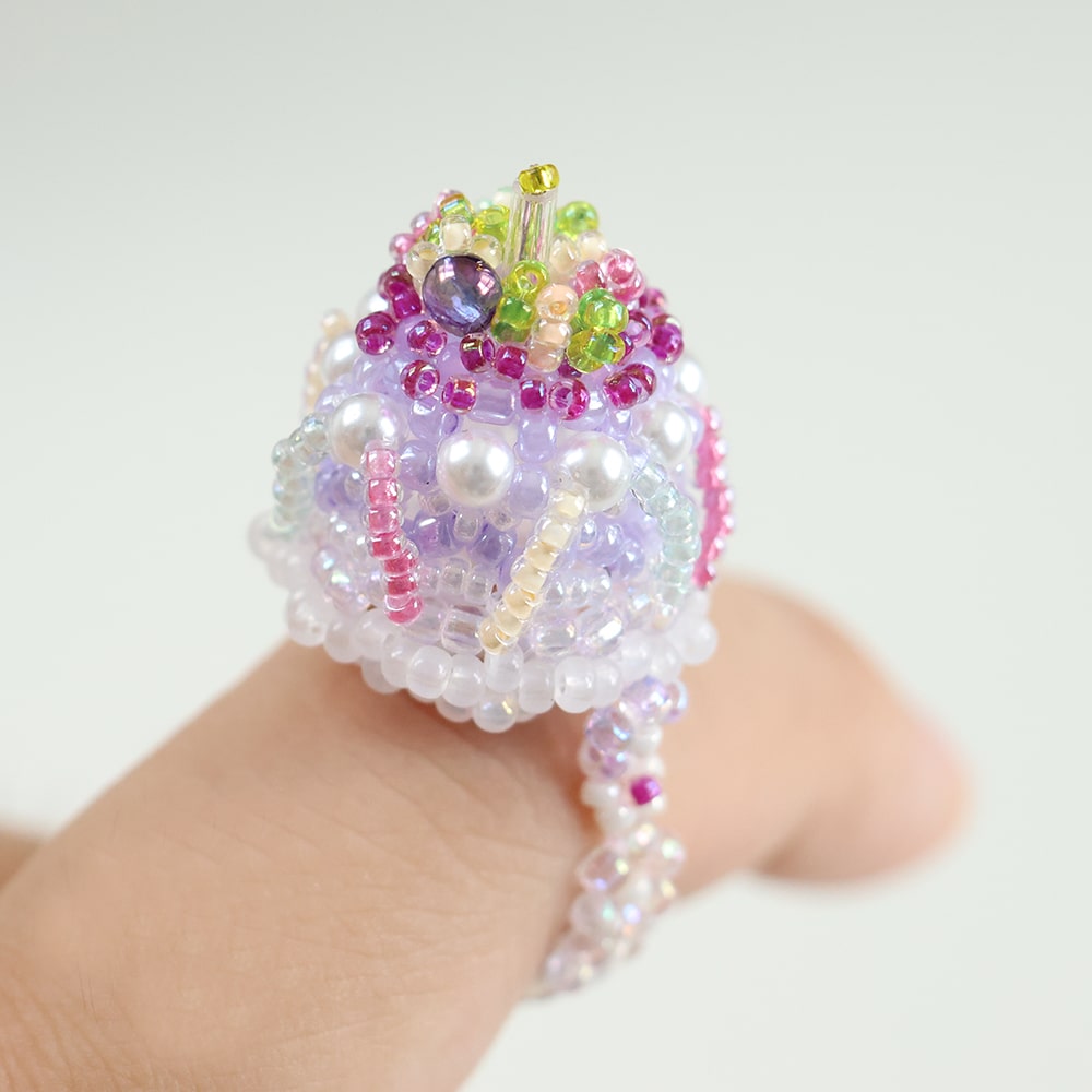 Colorful beaded cake ring on a hand against a white background