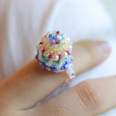 Colorful beaded rainbow cake ring on a finger with a blurred background