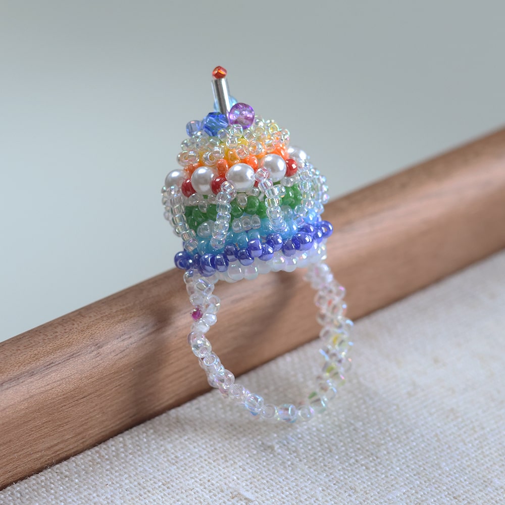 Colorful beaded cupcake ring on a wooden stick with a neutral background