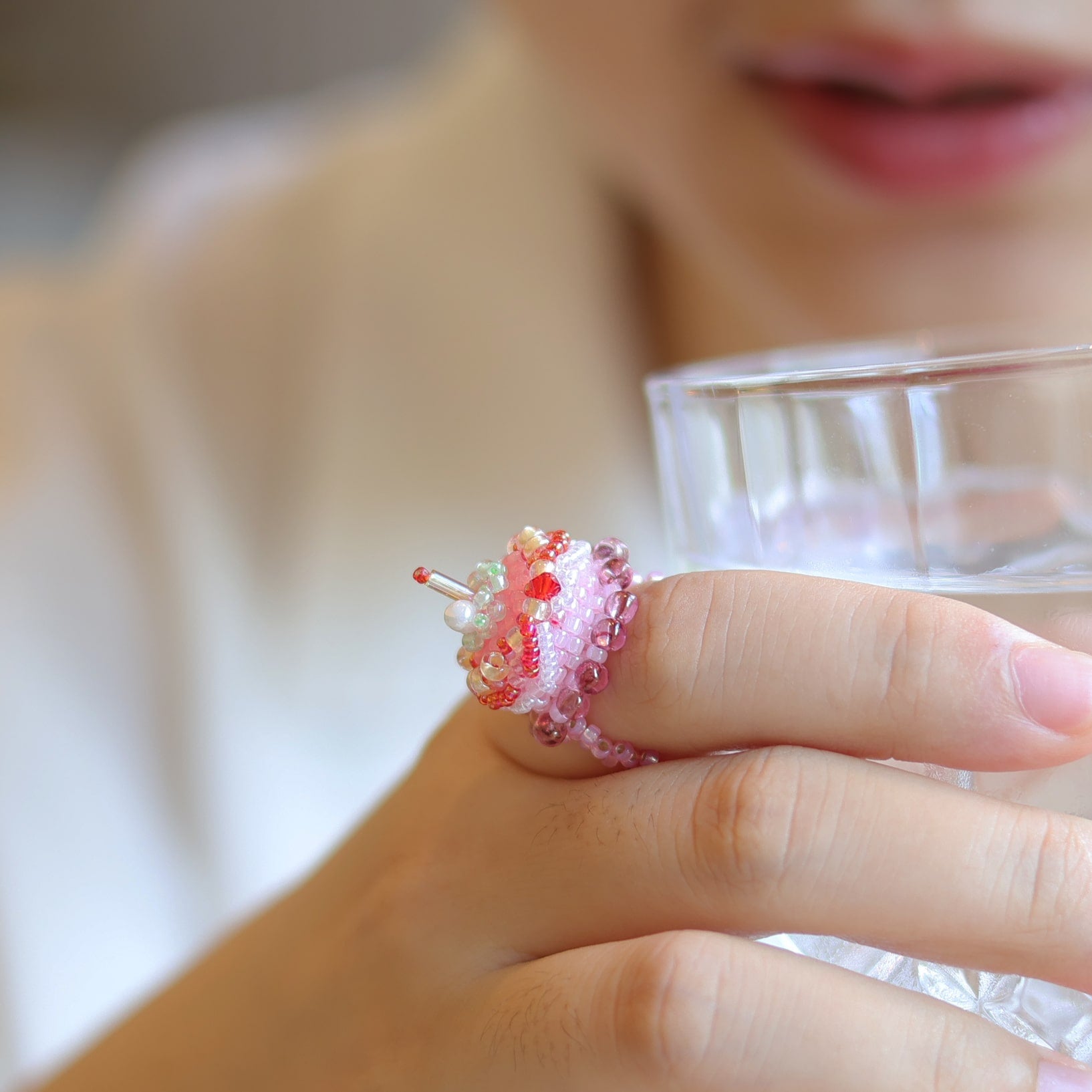 Person wearing a decorative cake ring with a small cake design on a blurred background