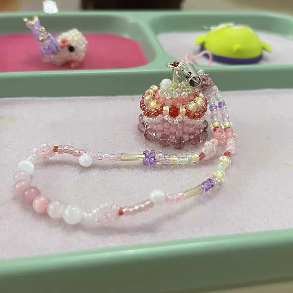 Colorful beaded phone charm on a pink surface with a green tray in the background
