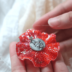 Red beaded flower brooch held between fingers against a neutral background