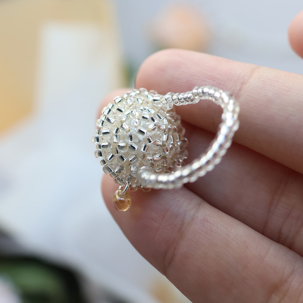 Silver beaded pudding ring held between fingers against a blurred background