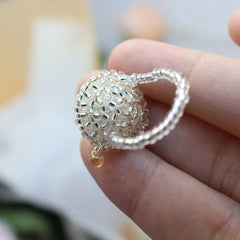 Silver beaded pudding ring held between fingers against a blurred background