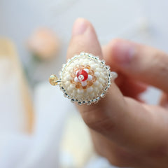 Close-up of a hand wearing a decorative beaded ring with a red center.