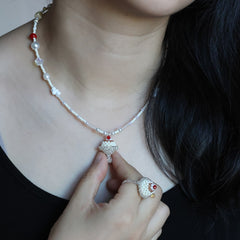 Close-up of a person wearing a pearl necklace with a hand adjusting it, against a dark background.